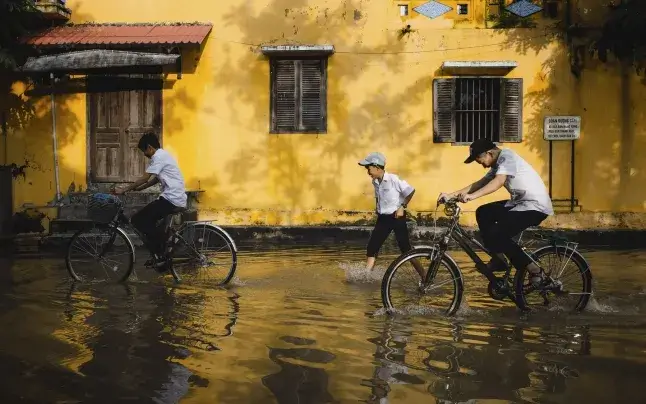 Children cycling on a street flooded by rain.