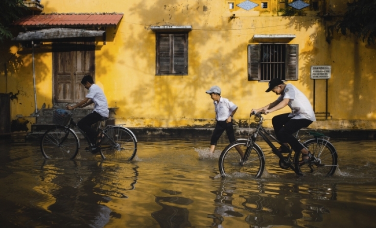 Children cycling on a street flooded by rain.