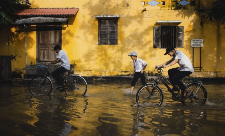 Children cycling on a street flooded by rain.