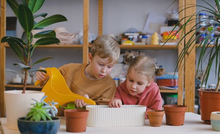Two children watering a plant. 